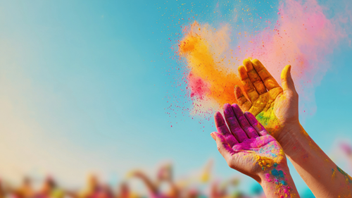 Hands throwing purple and yellow powder into a clear blue sky