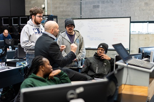An instructor teaches a group of four students in a computer lab